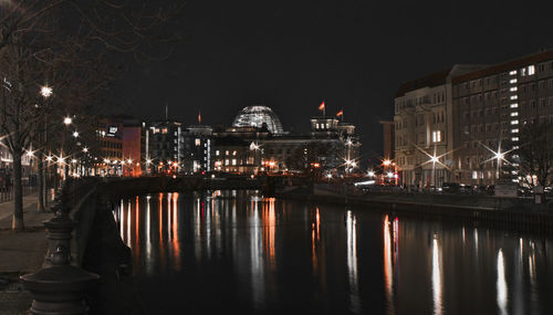 Illuminated buildings by river against sky at night