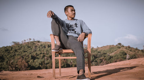 Young man sitting on chair against sky