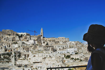 Rear view of man looking at city buildings against clear blue sky