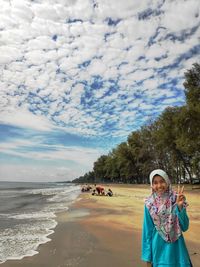 Portrait of girl gesturing peace sign while standing at beach against sea