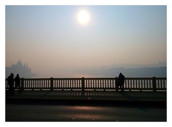 Silhouette people walking on bridge over sea against clear sky