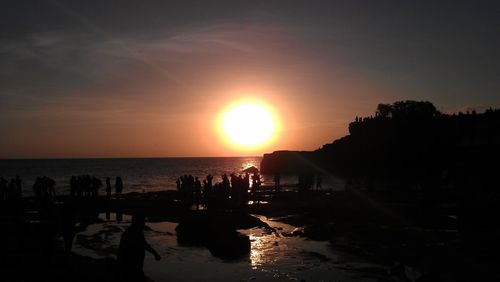 Silhouette people on beach against sky during sunset