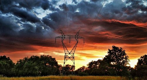 Silhouette trees and electricity pylon against dramatic sky during sunset