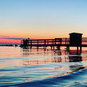 Silhouette pier on sea against clear sky during sunset