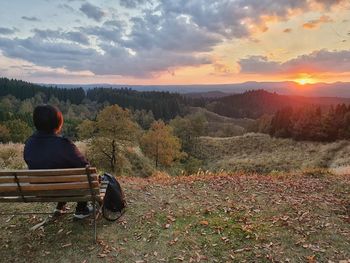 Rear view of woman sitting on bench looking at tree mountains during sunset