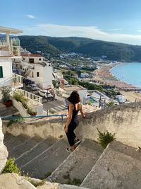 Rear view of woman sitting on rock by sea against sky