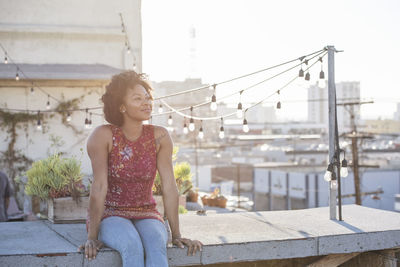 Young woman sitting on rooftop terrace, enjoying the sun