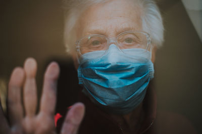 Close-up portrait of senior woman wearing mask looking through window