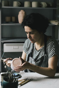 Mature female owner concentrating while painting cup in workshop