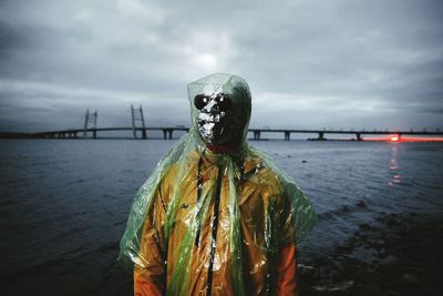 Man wearing mask while standing against sea during sunset