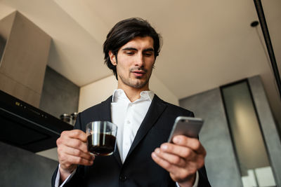 Businessman holding coffee cup while using mobile phone