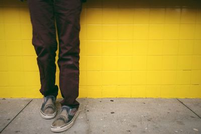 Low section of man standing on yellow wall