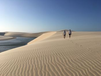 Men walking on sand dune in desert against blue sky