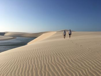 Man walking on sand dune in desert against clear blue sky