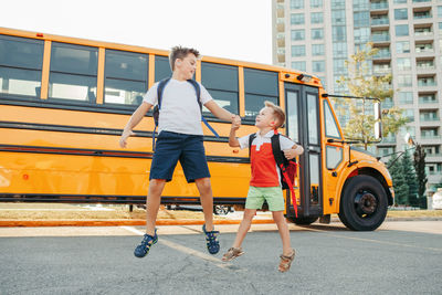 Cheerful brothers jumping against school bus