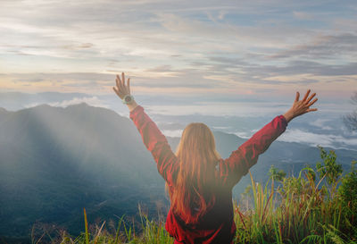 Rear view of woman with arms raised against sky