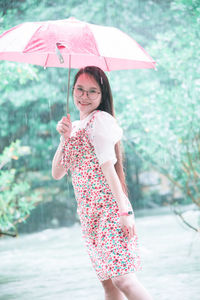 Portrait of smiling young woman holding umbrella standing by river