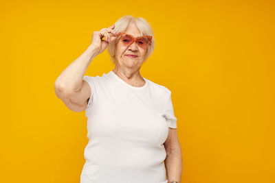 Portrait of senior woman standing against yellow background