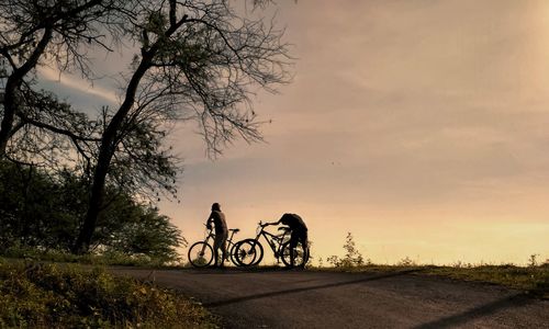 Bicycles riding bicycle on road against sky at sunset