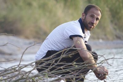 Portrait of mid adult man collecting stones while crouching at beach