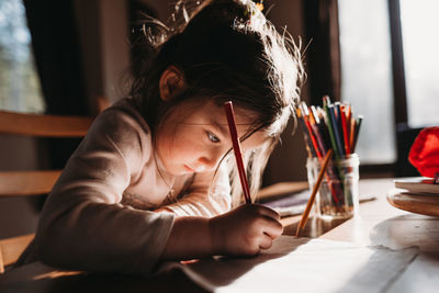 Girl drawing with colored pencil on paper while sitting at table