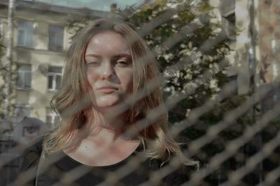Portrait of beautiful young woman seen through chainlink fence