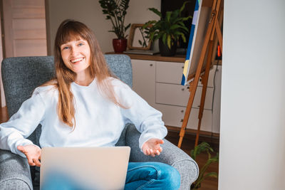 Portrait of smiling woman using laptop while sitting at home