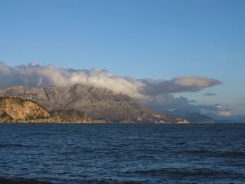 Scenic view of sea by mountain against sky