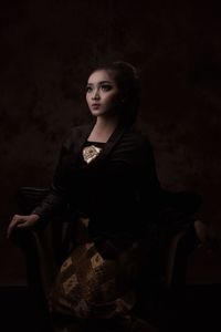 Beautiful young woman sitting on chair in dark room