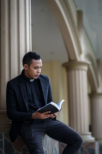 Young man reading bible standing by column