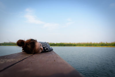 Woman lying on pier over lake against sky