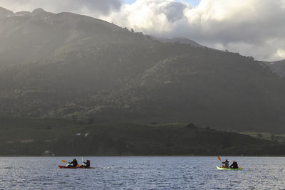 People on boat in sea against mountains