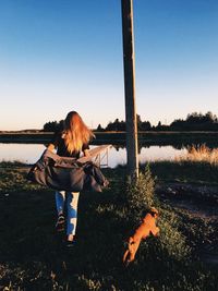 Rear view of woman with dog by lake against sky