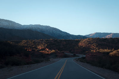 Road leading towards mountains against clear sky