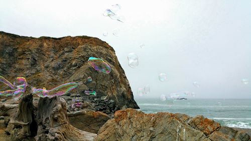 Bubbles against rock formation in sea against sky