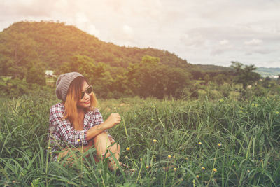 Woman sitting on grassy field against sky