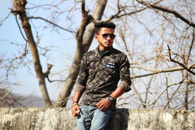 Portrait of young man wearing sunglasses standing against trees