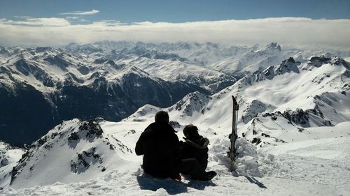 Rear view of friends sitting on snowcapped mountain against sky