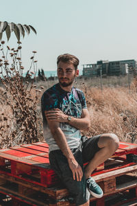 Portrait of young man sitting on field against clear sky