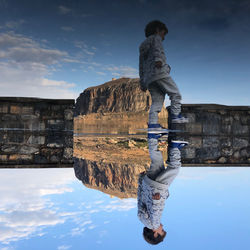 Reflection of man standing on water against sky