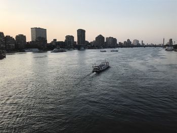 Boats sailing in river against cityscape during sunset