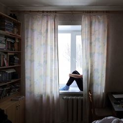 Woman sitting behind curtain at home