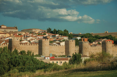 Stone towers with large wall over the hill, encircling the avila houses at sunset, in spain.