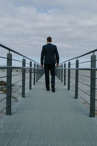 Rear view of businessman walking on pier over sea against sky