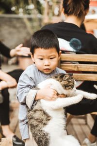 Cute boy with cat sitting on bench outdoors