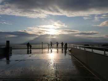 Silhouette people standing by railing against sky during sunset