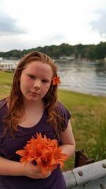 Portrait of teenage girl with orange lilies against lake