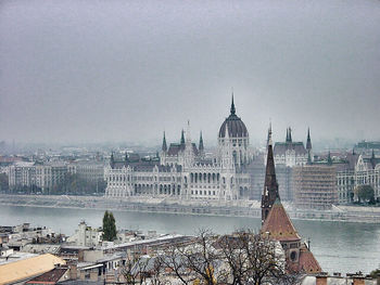 Hungarian parliament building by danube river against sky in city