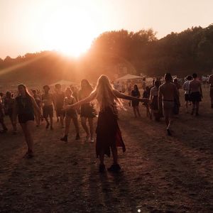 Group of people enjoying on field against sky during sunset