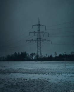 Electricity pylon on snow covered field against sky